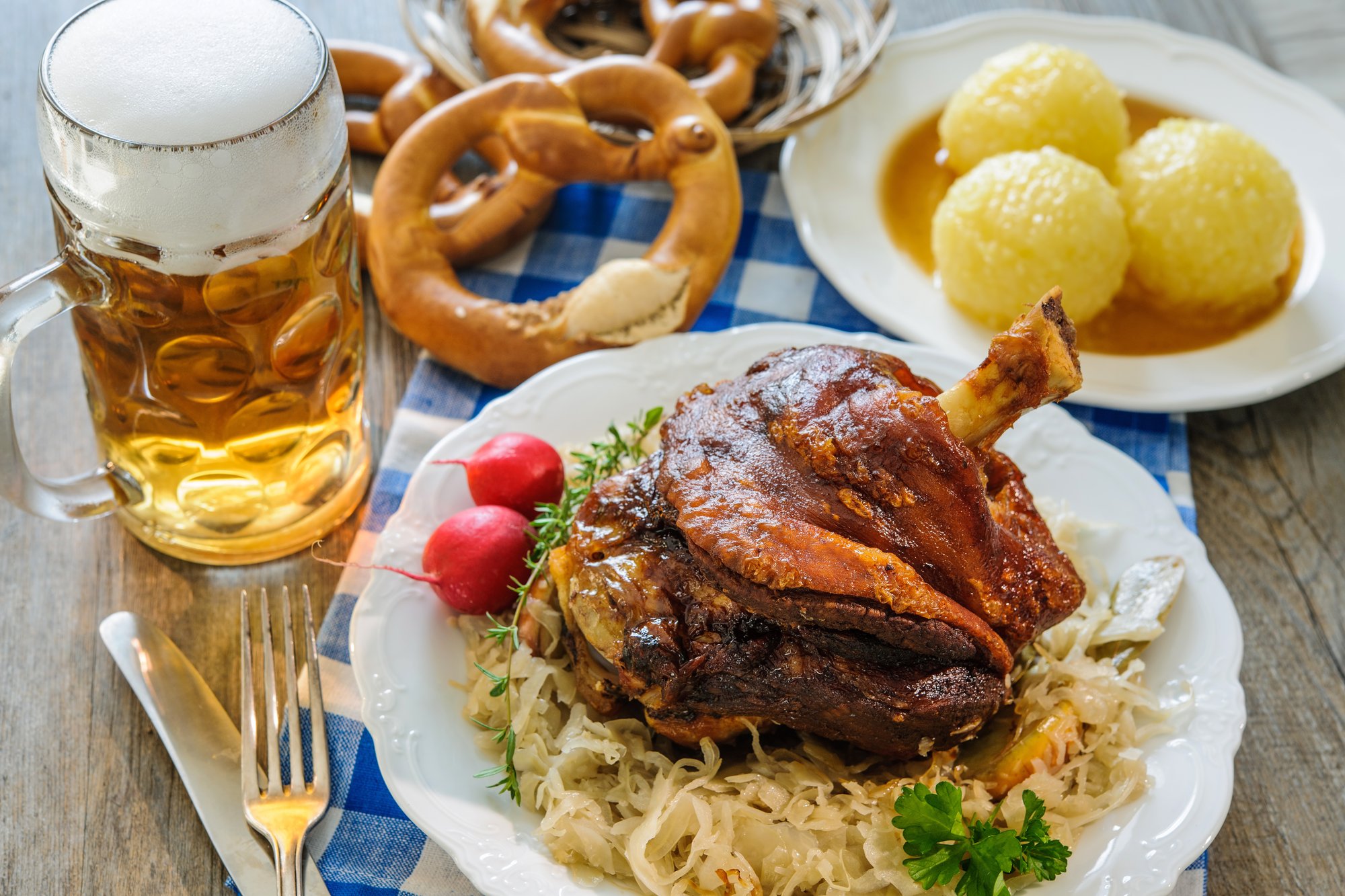 Traditional Bavarian food platter of roast pork knuckle with dumplings and sauerkraut, soft pretzels, and a stein of beer